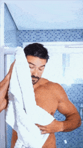 a shirtless man wipes his face with a white towel in a bathroom