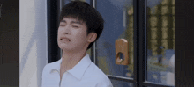 a young man in a white shirt is making a funny face while standing in front of a window .