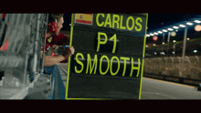 a man holding a sign that says carlos p1 smooth on it