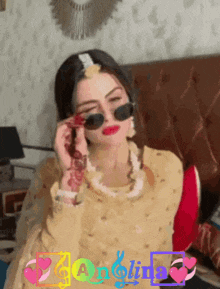a woman wearing sunglasses is sitting on a couch in front of a sign that says ' angelina '
