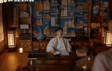a man in a traditional costume is sitting at a desk in a room with a lot of bookshelves .