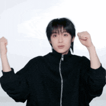 a young man wearing a black jacket is raising his fists in the air