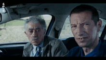 two men are sitting in a car with the letters rts on the bottom right