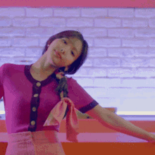 a woman in a pink top and pink skirt is dancing in front of a white brick wall