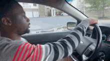 a man in a striped sweater is driving a kia