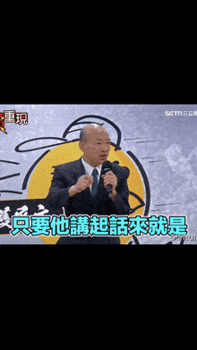 a man in a suit and tie is speaking into a microphone in front of a sign that says setn