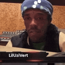 a man wearing a blue beanie is sitting in front of a sign that says lil uzivert