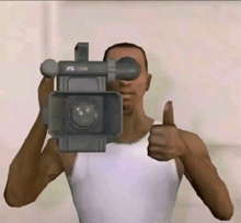 a man in a white tank top is holding a video camera in front of his face and giving a thumbs up