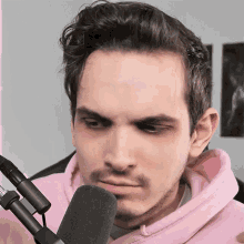a man in a pink hoodie stands in front of a microphone making a funny face