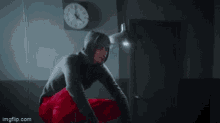 a man in a hoodie is squatting down in front of a clock that shows the time as 8:17