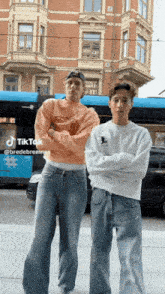 two men standing next to each other with their arms crossed in front of a building with tiktok written on the bottom