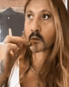 a woman with long blonde hair and a mustache is eating a chicken nugget .