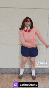 a woman in a pink sweater and blue skirt is dancing in front of a wall that says tik tok