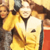 a man in a yellow suit is standing in front of a group of people and smiling .