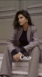 a woman in a suit is sitting on a set of stairs with the word coco on the bottom