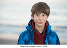 a young boy is wearing a blue jacket and a red hoodie .