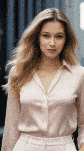 a woman wearing a pink shirt and white pants looks at the camera
