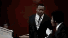 a man in a suit and tie is giving a speech at a podium while another man stands behind him .