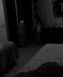 a couple of girls standing in a room with a purple blanket on a bed