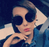 a woman wearing round sunglasses and a denim jacket is sitting in a car