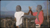 two people giving each other a high five in front of a fence