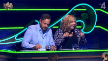 a man and a woman sitting at a table in front of a masked singer logo