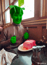a person with a green face is sitting at a table with a plate of cake