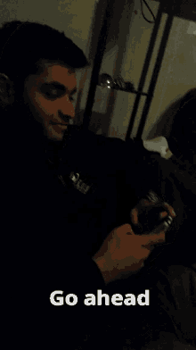 a man sitting on a couch holding a cell phone with the caption go ahead