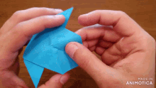 a person is holding a blue origami fish in their hands made in animotica