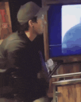 a man wearing a hat is looking at a tv screen