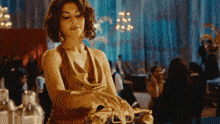 a woman in a gold dress is standing in a crowded room holding a purse .