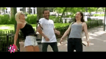 a man and two women are dancing in a park with the letter r in the corner