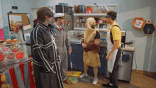 a man in a yellow apron is standing in a kitchen with other people