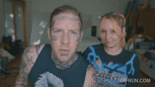 a man with a tattoo on his forehead is standing next to a woman wearing a shirt that says gifrun.com