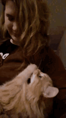a woman holds a cat in her arms and the cat is looking up at the camera