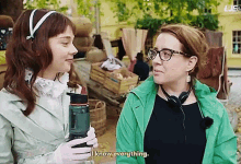 a woman in a green jacket is talking to another woman who is holding a water bottle ..