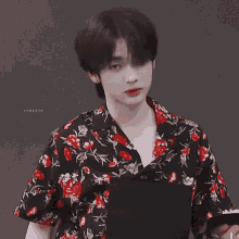a young man wearing a black shirt with red and white flowers on it