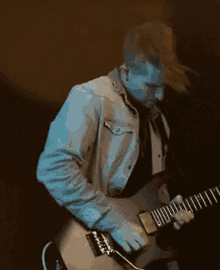 a man in a denim jacket is playing an electric guitar in a dark room .