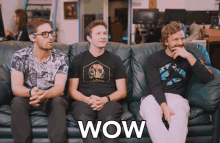 three men are sitting on a couch with the word wow written on the couch