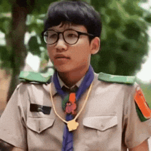 a young man wearing glasses and a scout uniform is standing in front of trees .