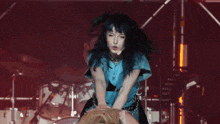 a woman with blue hair is dancing on a stage with a drum set in the background
