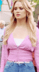a woman wearing a pink cardigan and blue jeans is walking down a street .