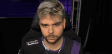 a man with blonde hair and a beard is sitting in a purple and black chair .