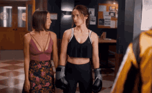 a woman wearing boxing gloves stands next to another woman in a gym