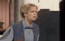a woman in a blue vest and bow tie is standing in a room .