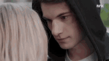 a close up of a man and a woman looking at each other . the man is wearing a black hoodie .