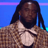 a man with dreadlocks is wearing a plaid jacket with pearls and a bow tie