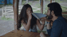a man and a woman are sitting at a table and the man is holding a piece of paper to his face