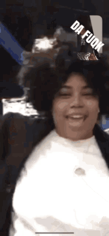 a woman wearing a white shirt and a black jacket is smiling with da fuok written on the screen behind her