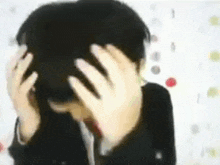 a person is covering their face with their hands and looking at the camera .